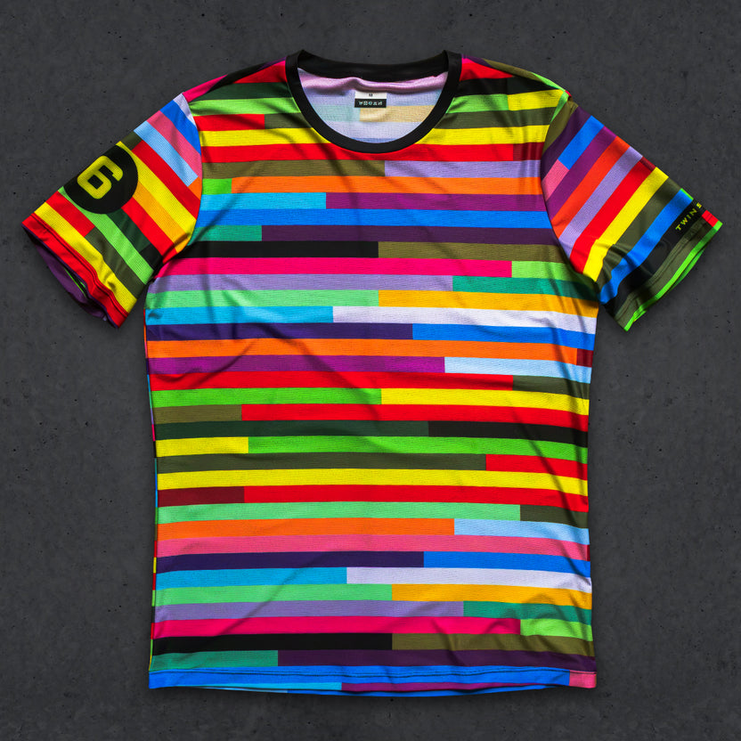 A short-sleeve crewneck t-shirt featuring a vibrant, multicolored horizontal stripe pattern with varying widths, laid flat on a dark textured background. The left sleeve features a black circle with a yellow stylized 'G' logo, and the inner collar label shows the brand 'G-DRIVE'.